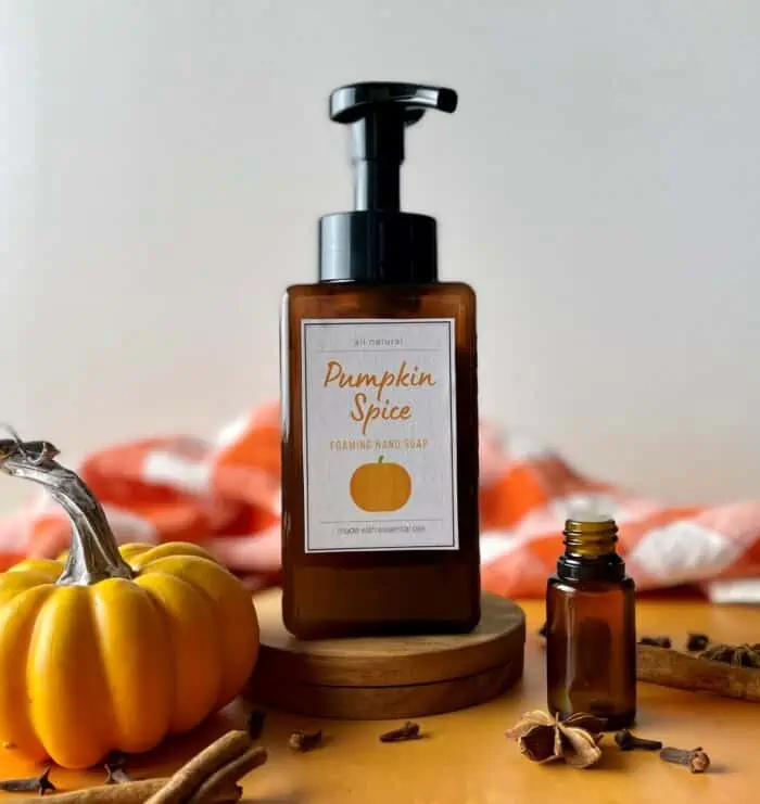 homemade pumpkin spice foaming soap made with essential oils -- small pumpkin, essential oil bottle, cinnamon sticks, cloves, star anise, and checkered orange towel