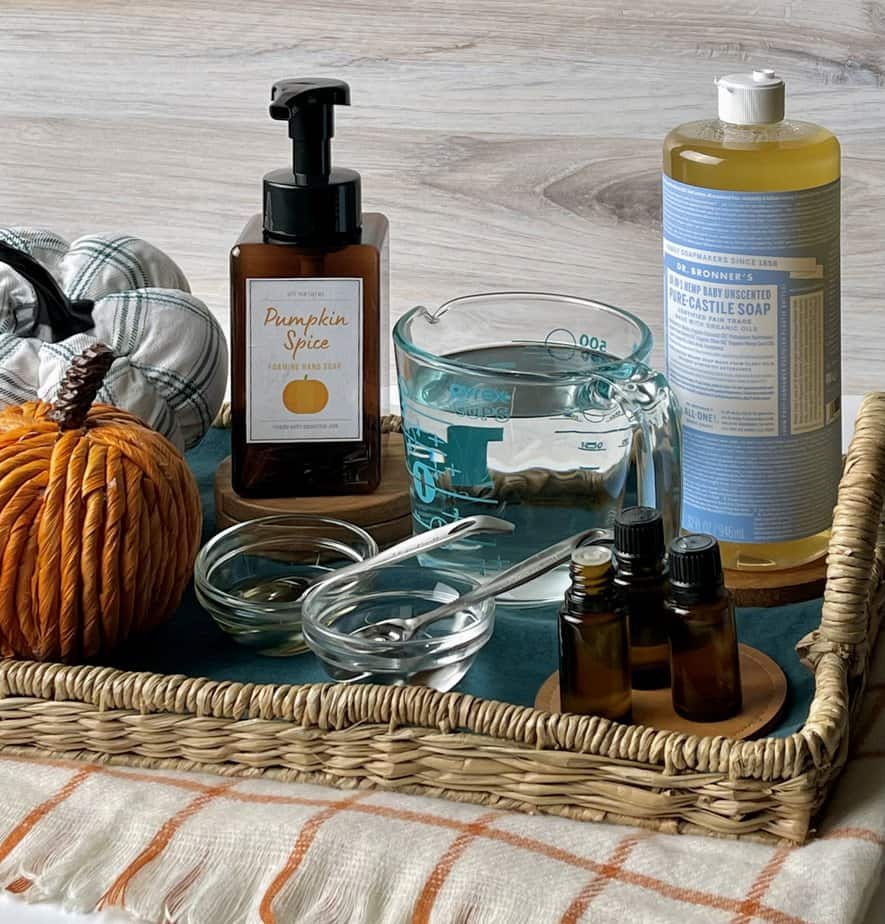supplies to make homemade foaming soap in fall scents -- liquid Castile soap, water, essential oil bottles, vegetable glycerin, and sweet almond oil on tray with decor pumpkins