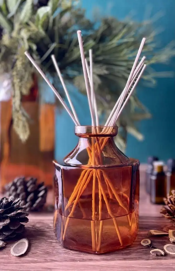 essential oil bottles, pinecones, and wood slices around amber glass reed diffuser