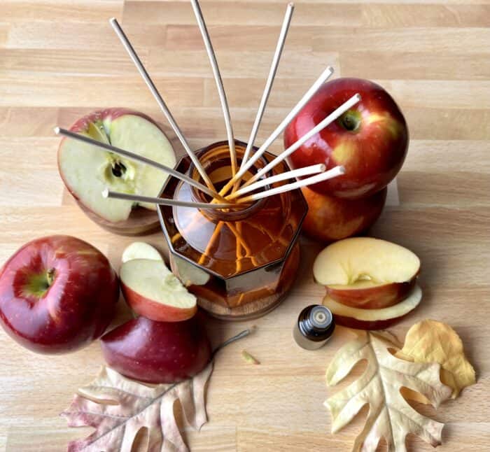 essential oil bottle, apples and apple slices around amber glass reed diffuser