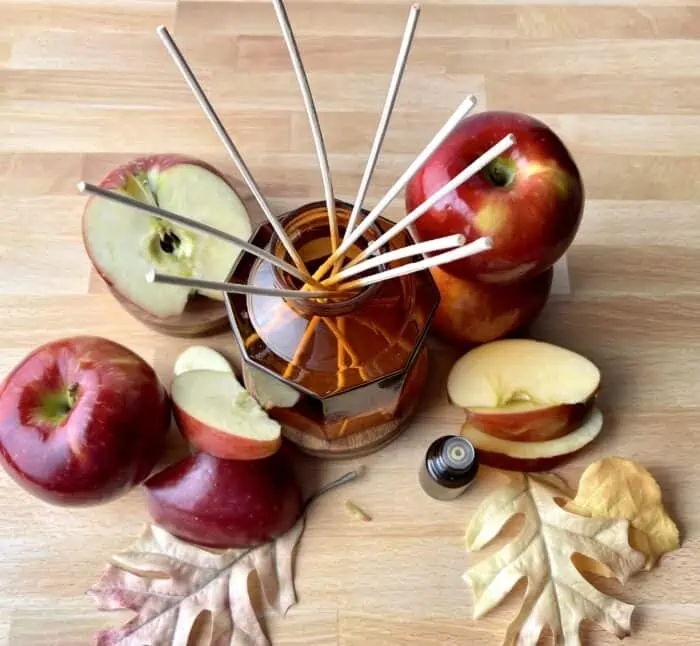 essential oil bottle, apples and apple slices around amber glass reed diffuser