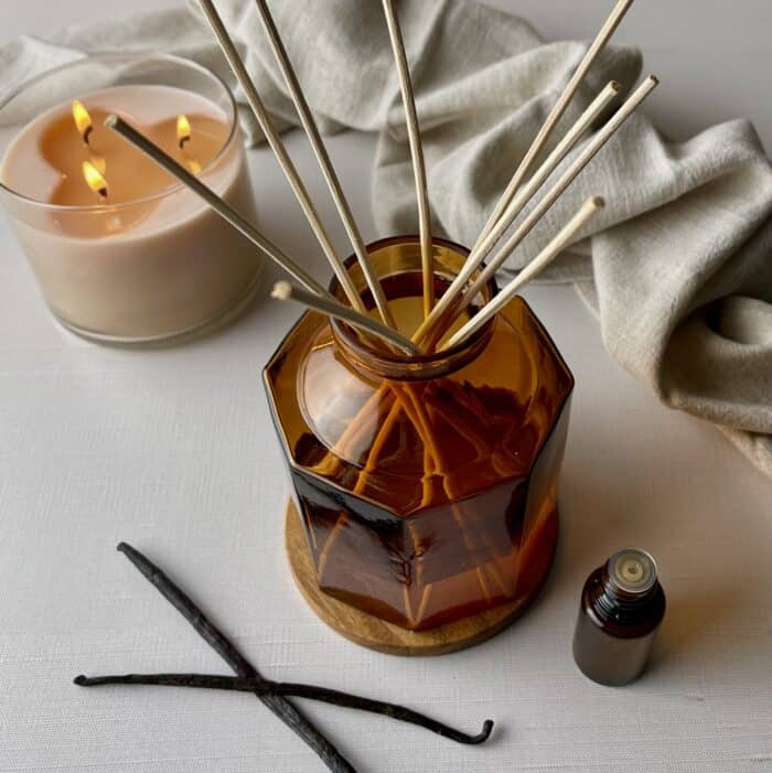 vanilla beans, essential oil bottle, and lit vanilla candle around homemade reed diffuser