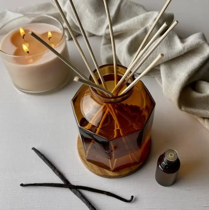 vanilla beans, essential oil bottle, and lit vanilla candle around homemade reed diffuser