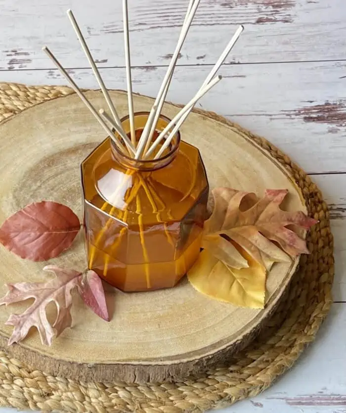 homemade reed diffuser with reed sticks and a few fall leaves on wood slice